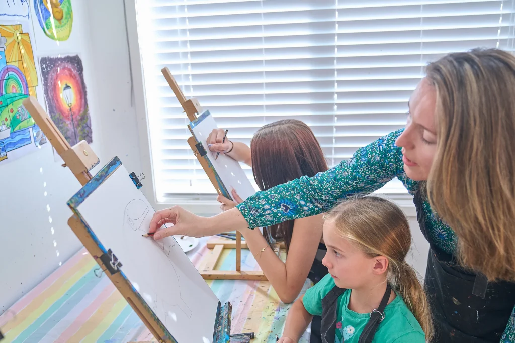 Two students at easels with Natalia leaning in to demonstrate — mid-class at the studio